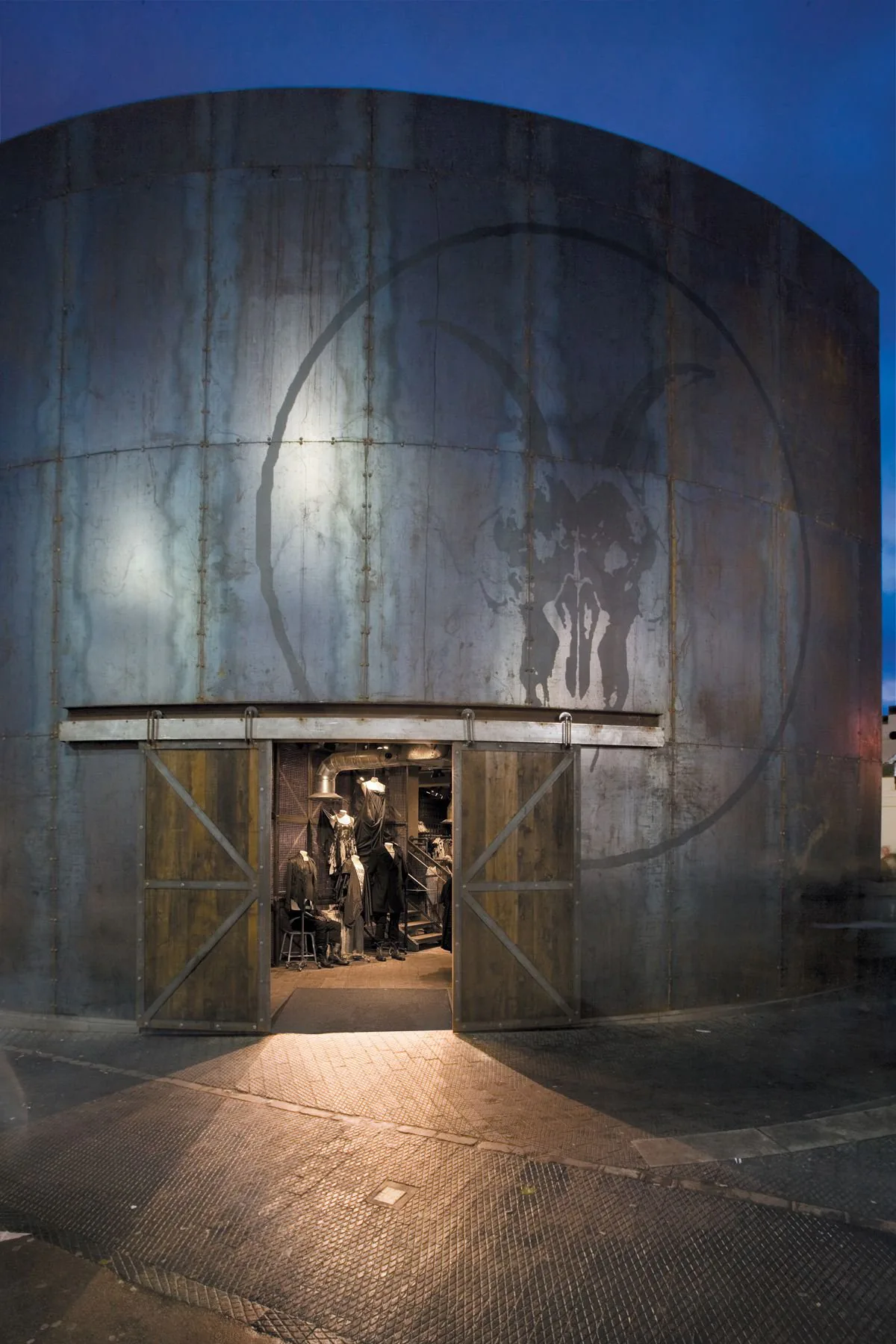 The AllSaints store entrance at night, behind a curved glass frontage.