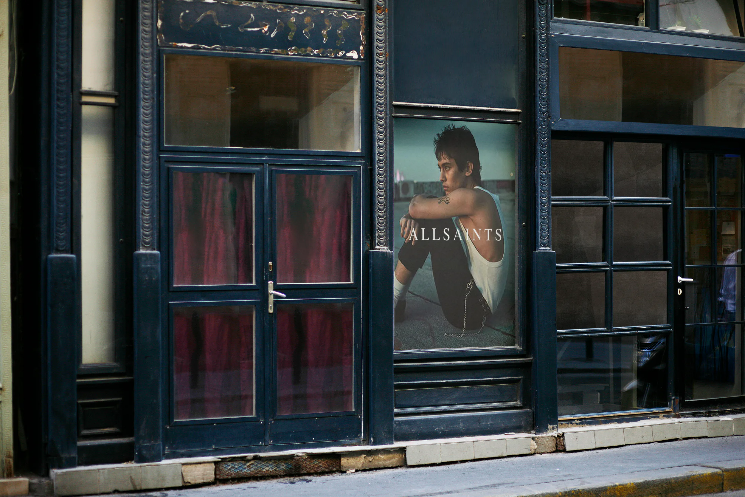 An AllSaints storefront with a campaign poster in the window.
