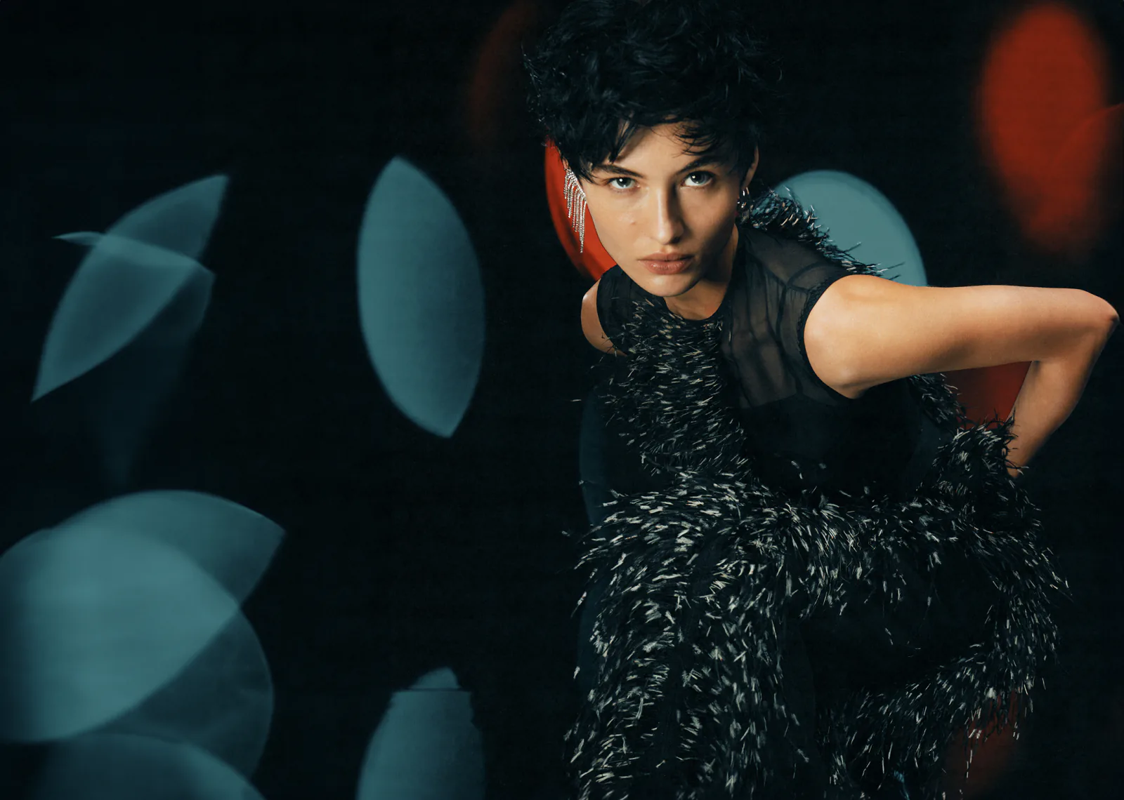 A woman in a black feathered top against dark teal, pale ovals floating behind her.