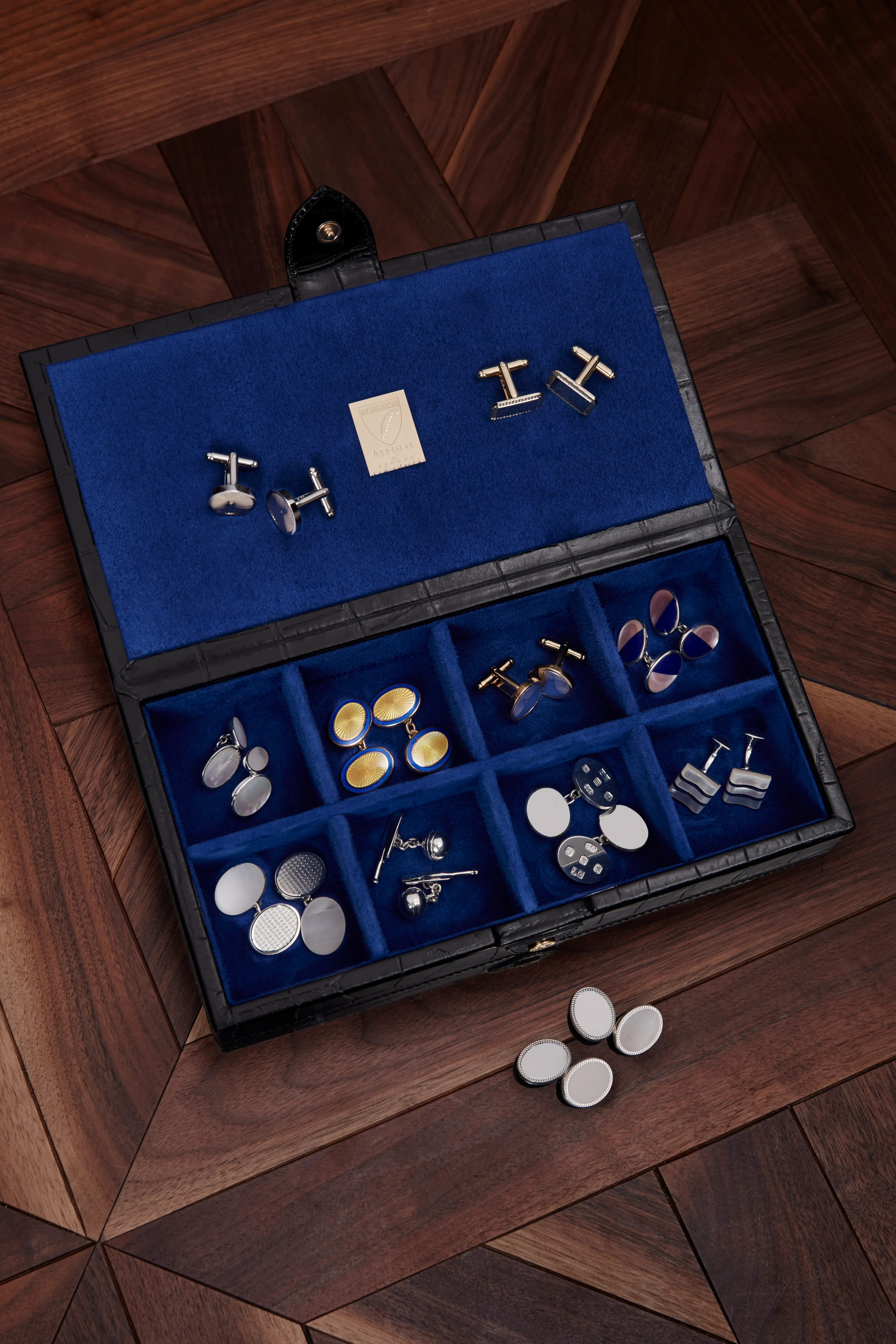 An open cufflink box lined in blue velvet, its pairs laid out in the tray.