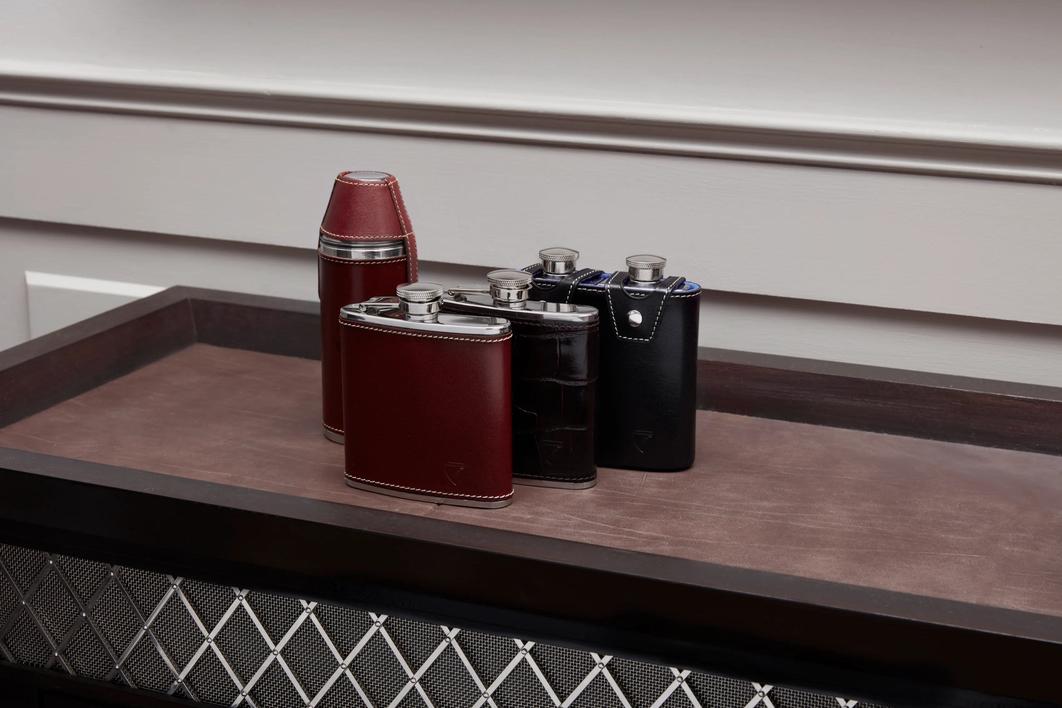 Four leather-cased hip flasks in a row on a suede tray.