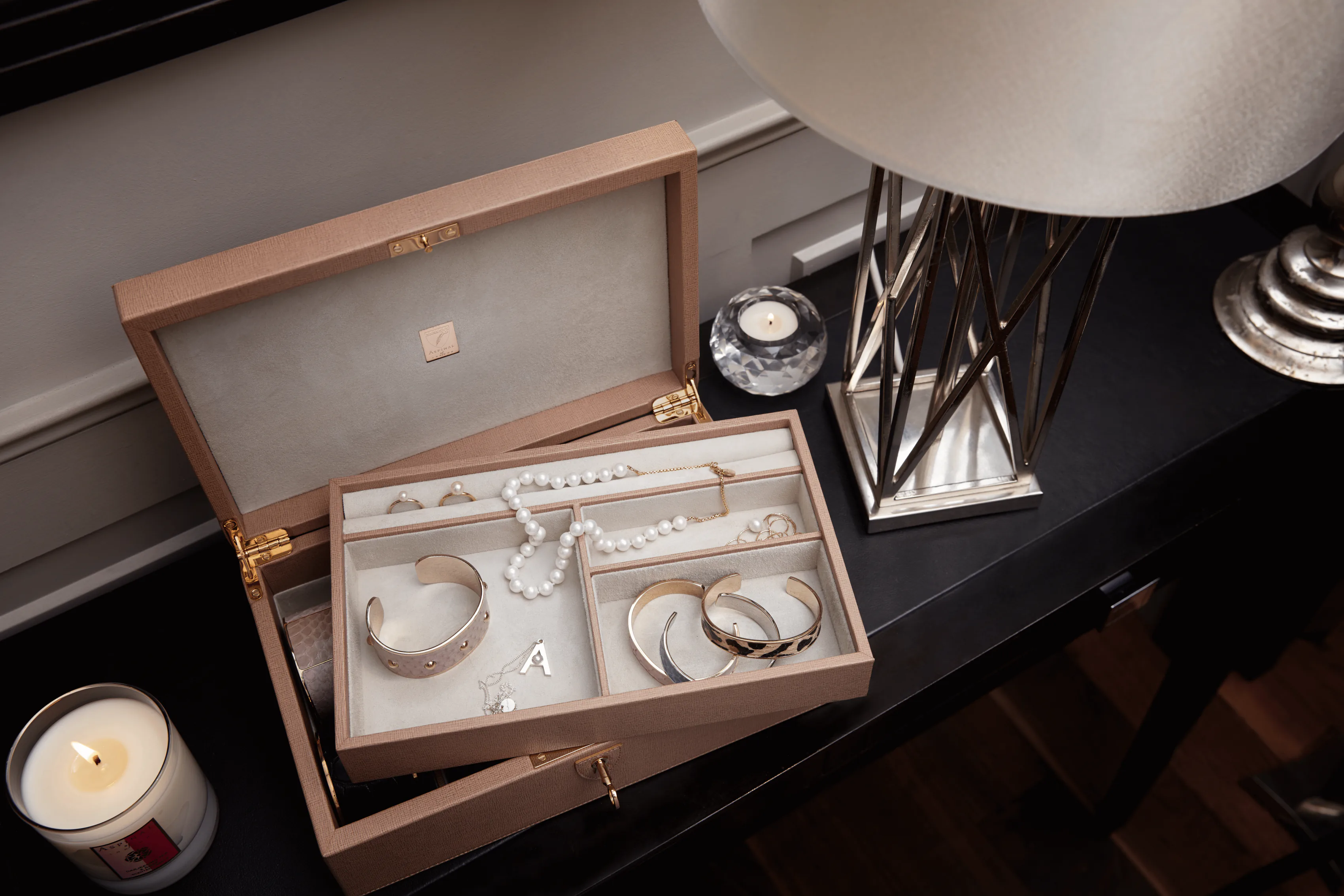 An open jewellery box on a dark table, rings and bangles in its compartments.