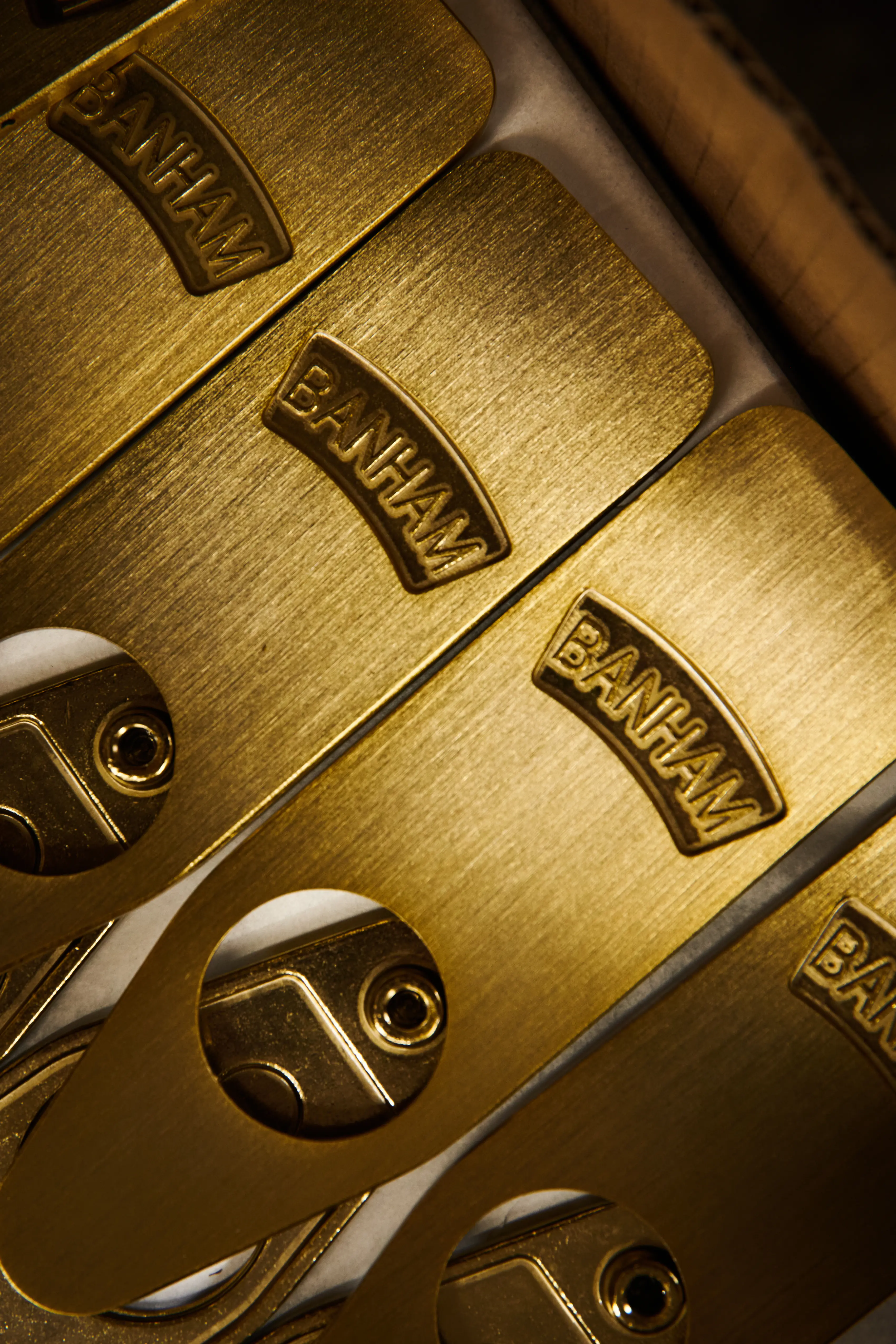 Brushed brass Banham lock covers stacked in a box, each raised-stamped with the Banham name.