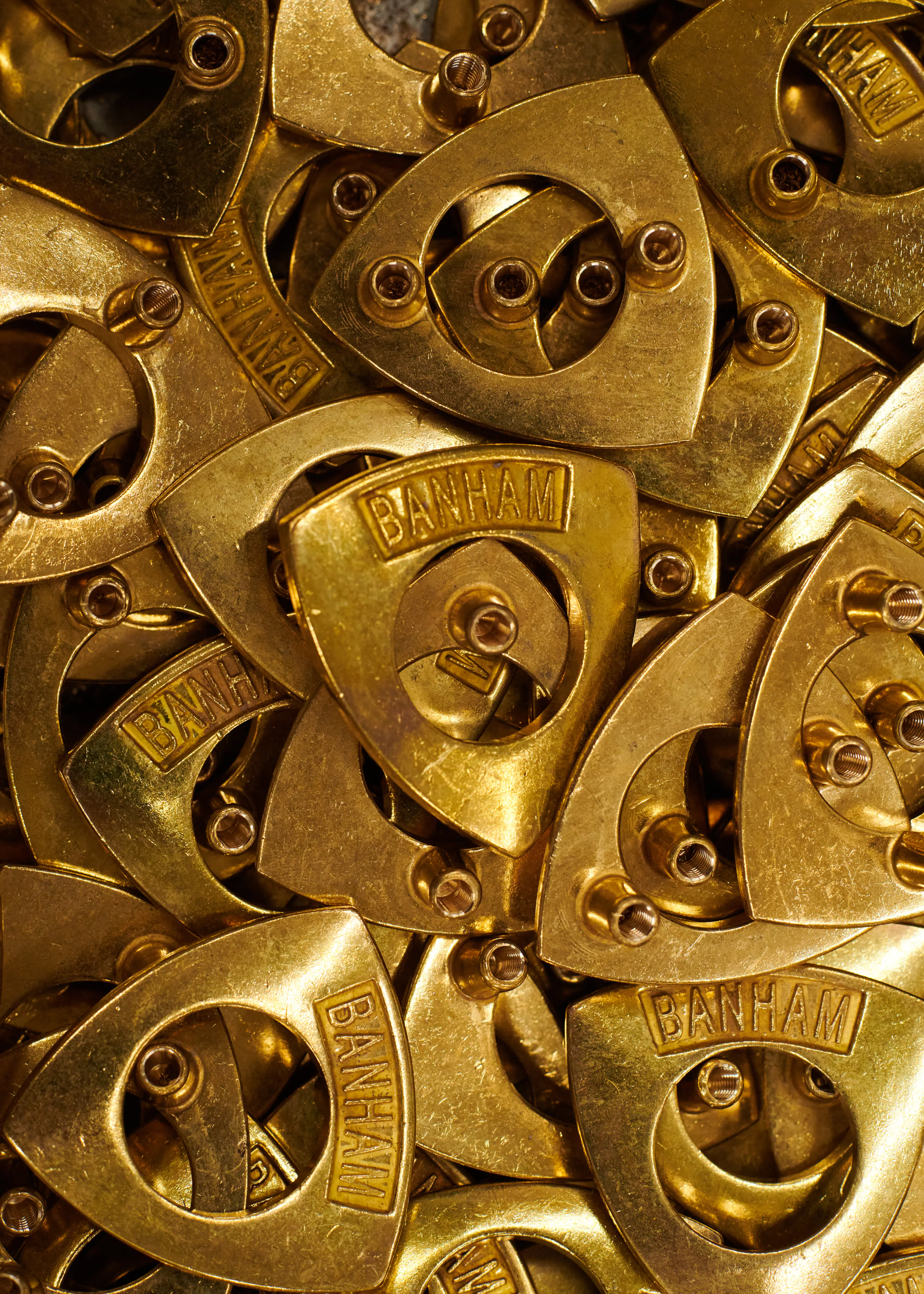 A pile of brass Banham shield escutcheons, each cast with the Banham name above its keyway.