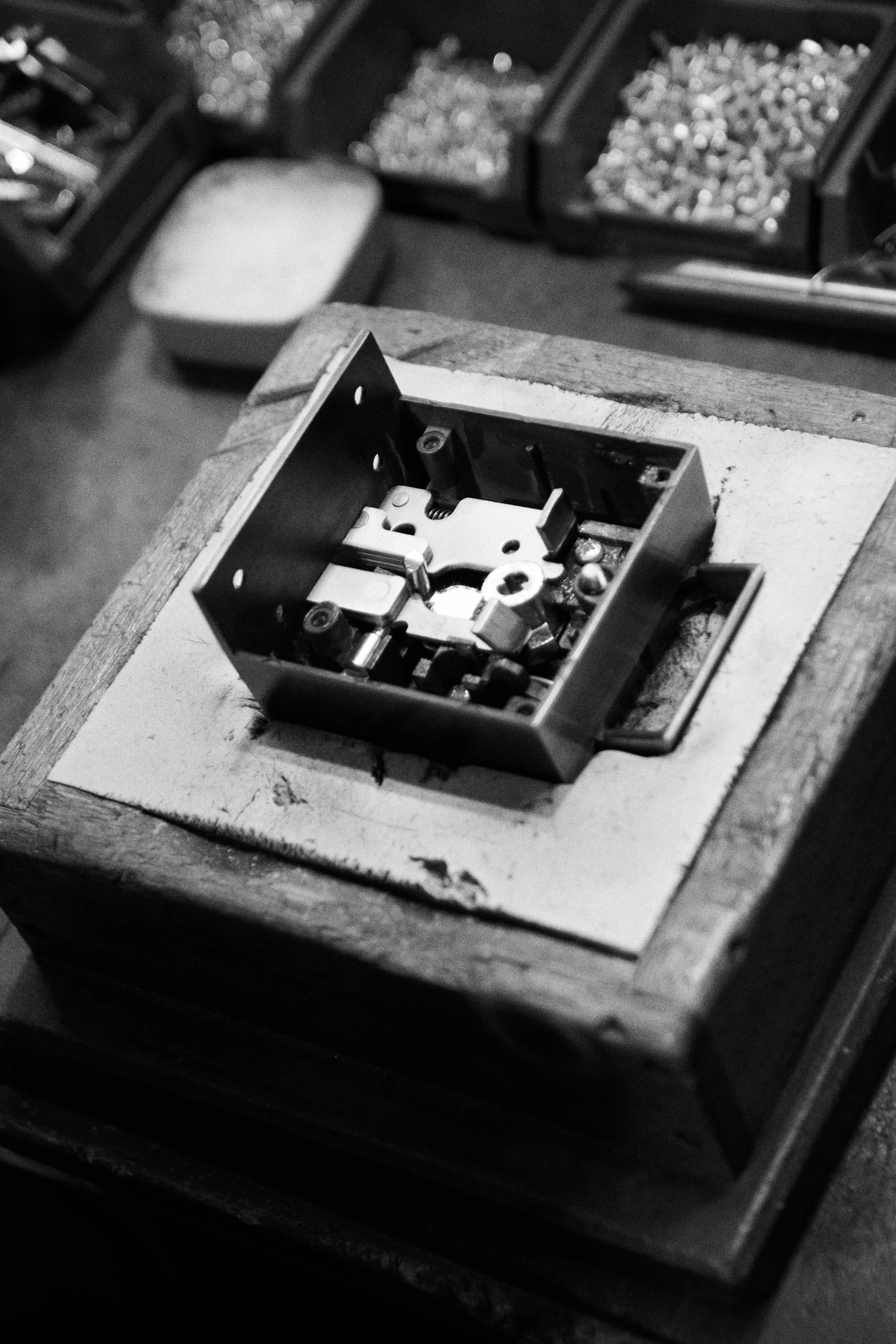 A part-assembled Banham lock case open in a wooden jig, its levers exposed, with trays of components behind.