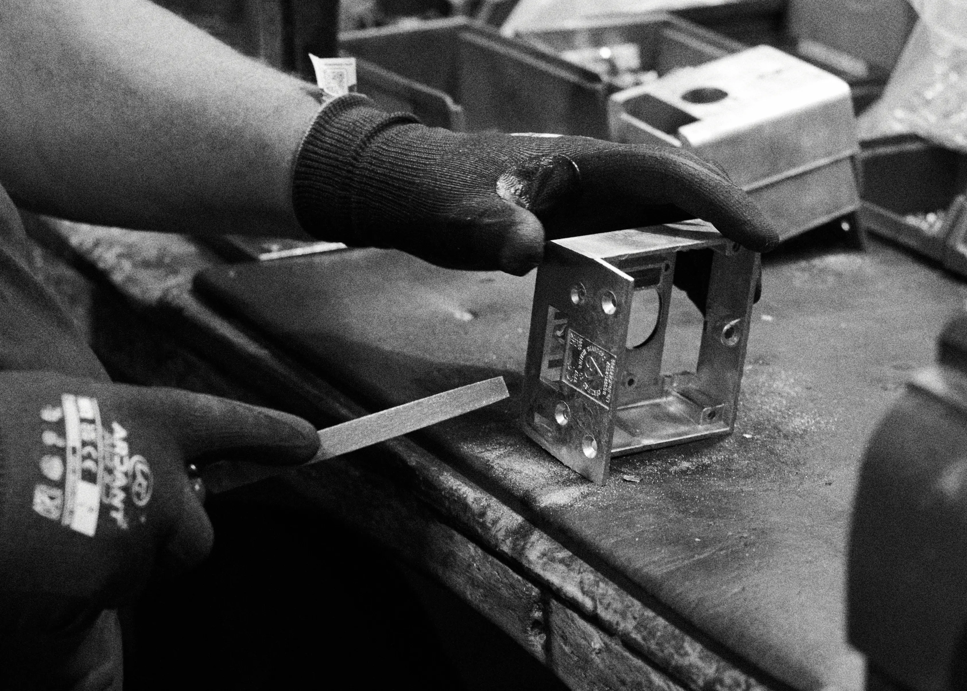 A Banham craftsperson steadying a machined lock case on the bench in one gloved hand, a flat file in the other.
