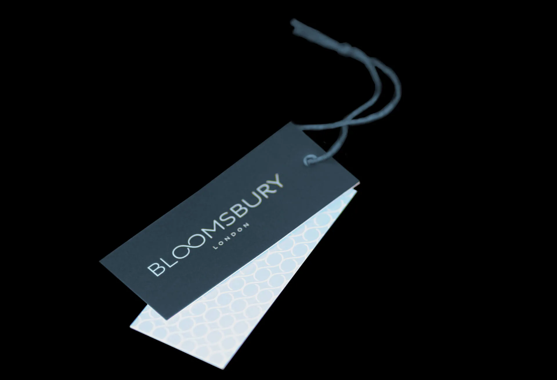 A teal swing tag on a cord, its patterned reverse showing behind.