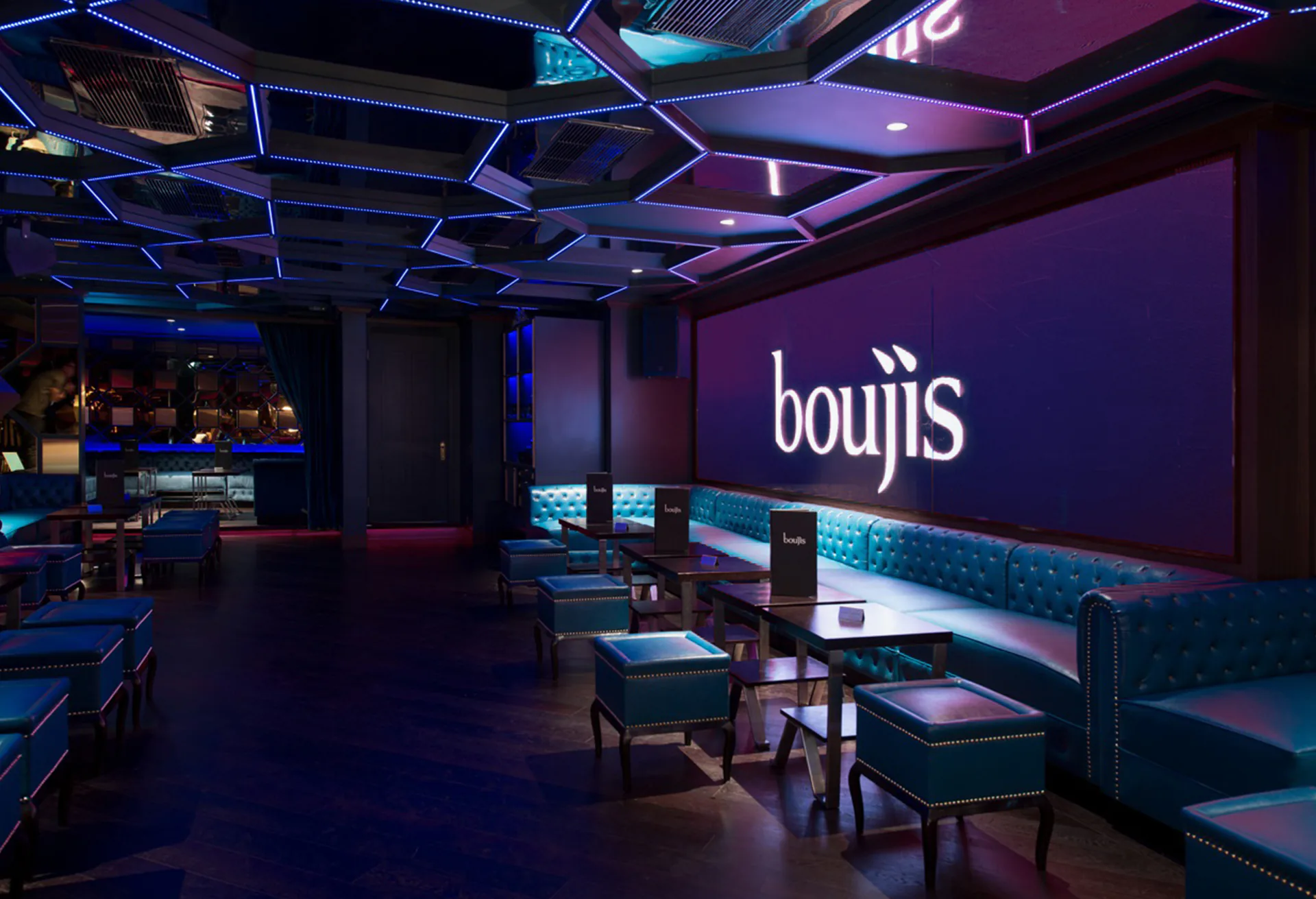 The bar and low stools beneath the boujis wordmark on a lit wall.