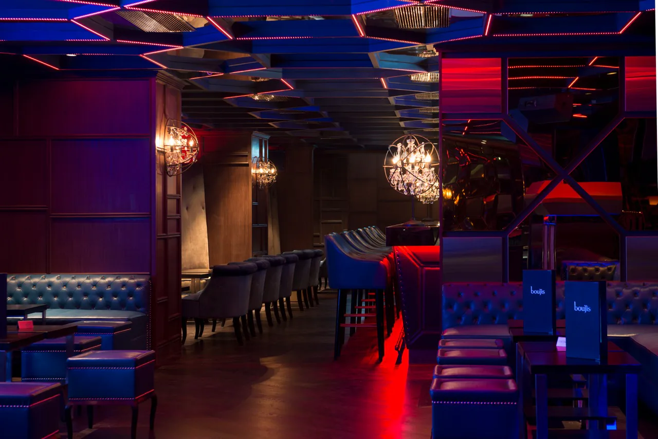 The club lit in red and blue, banquettes running back under low chandeliers.