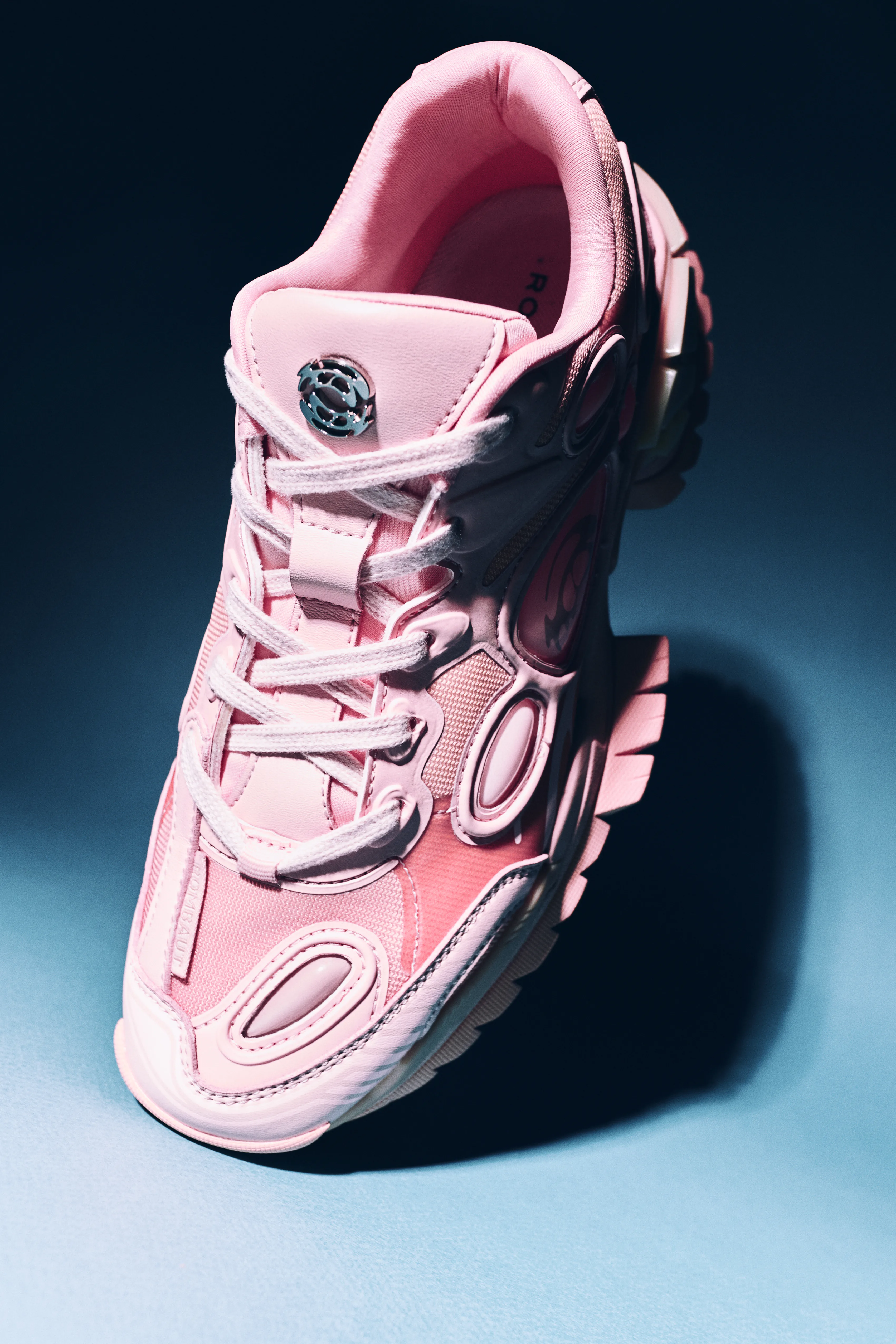 A pink chunky trainer lit against a blue and pink ground.