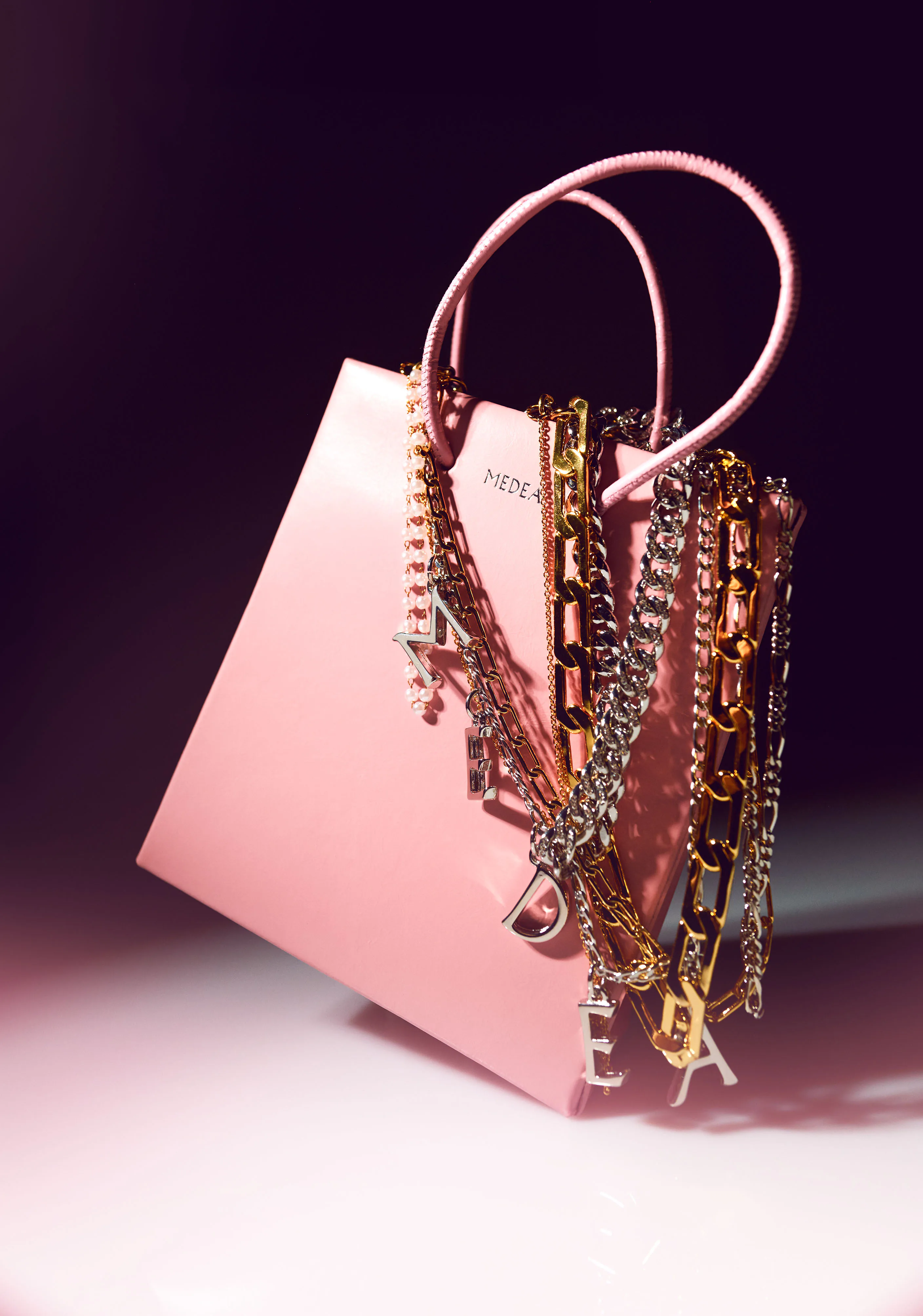 A pink tote hung with layered gold and silver charm chains.