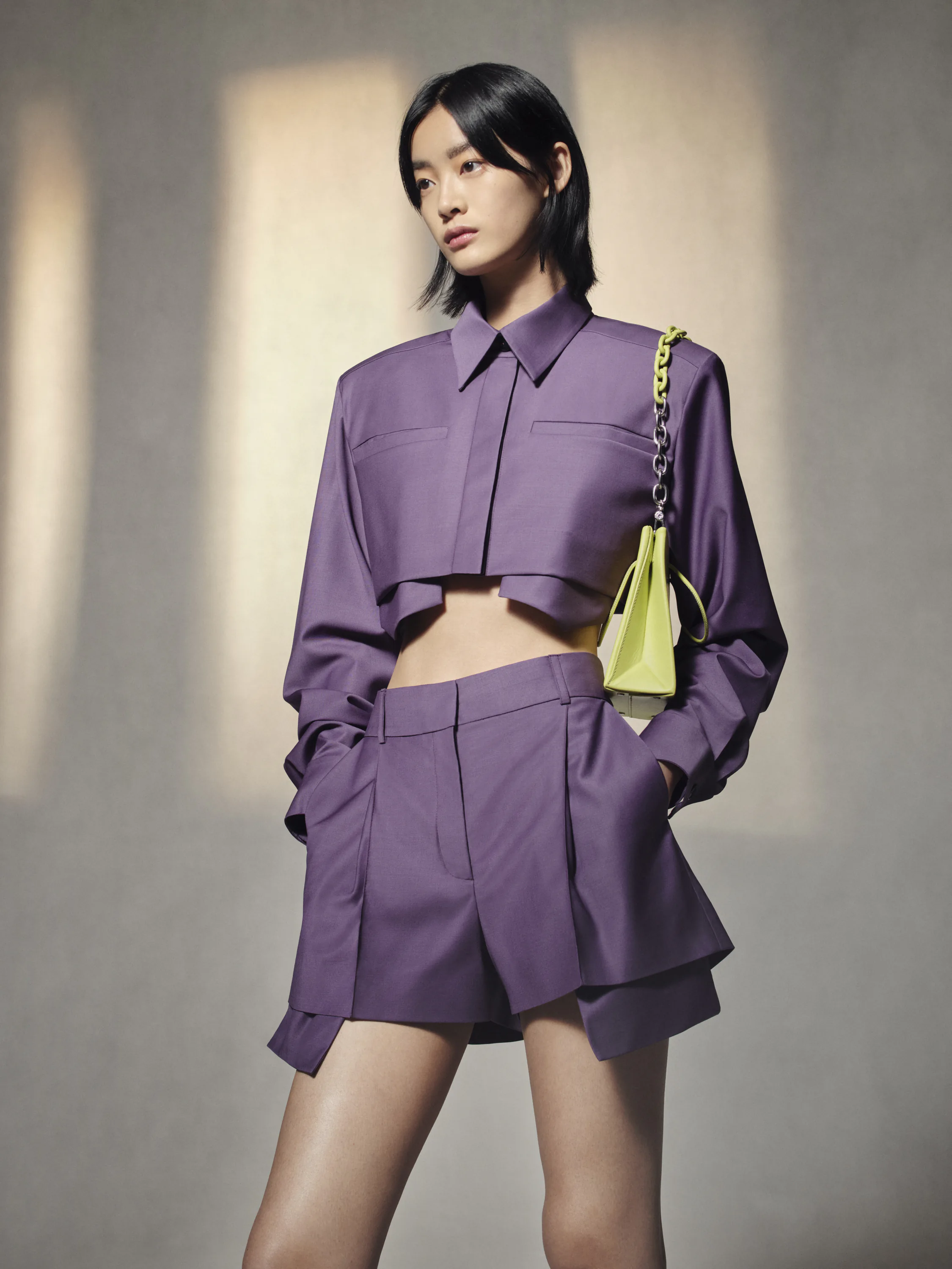 A model in a purple co-ord carrying a green bag.