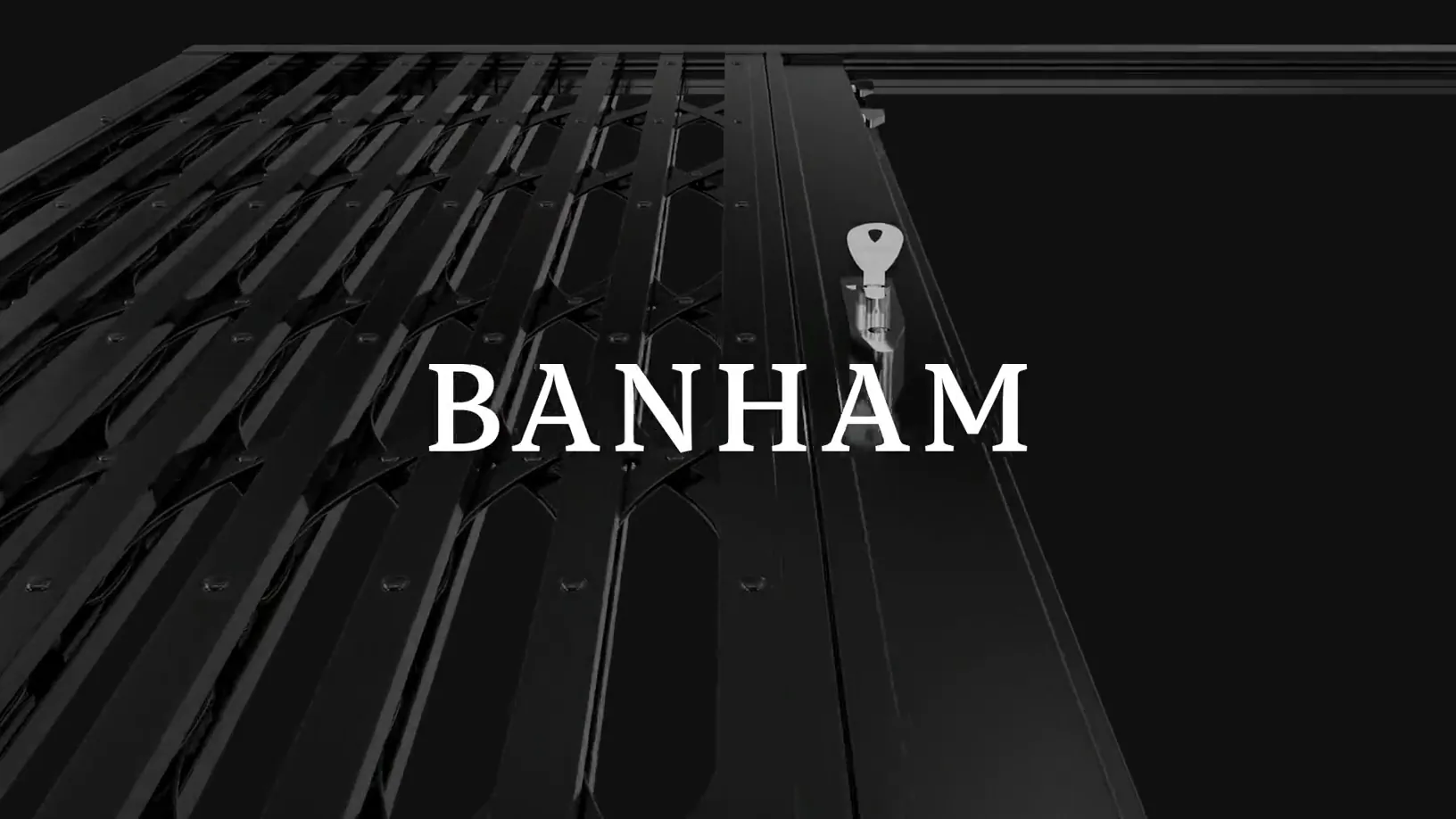 A black steel security gate seen along its length, a silver key standing in the lock cylinder, the Banham wordmark held in white across it.