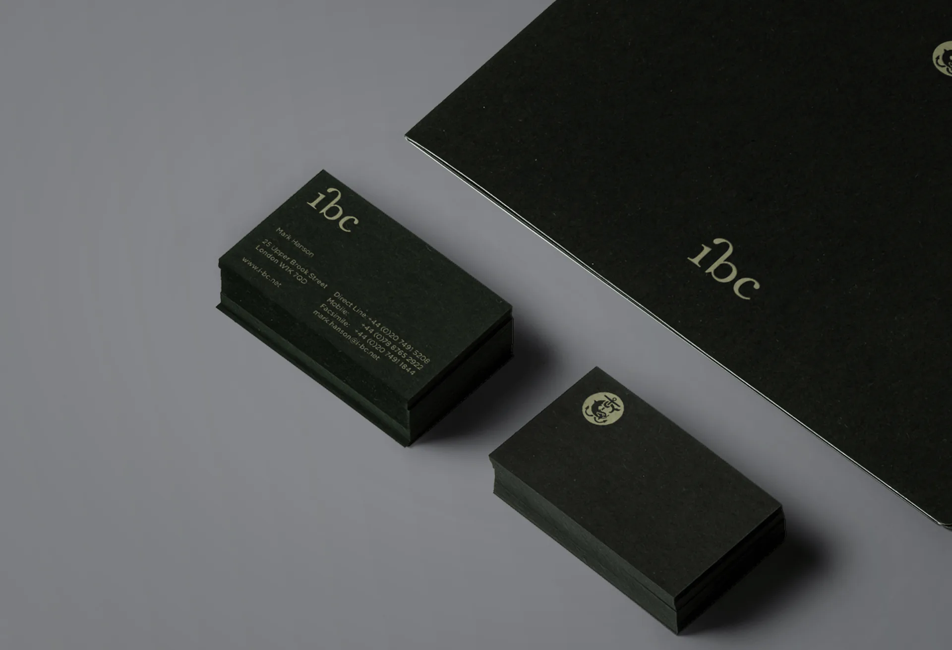 Two stacks of ibc business cards beside a black folder, on a grey surface.