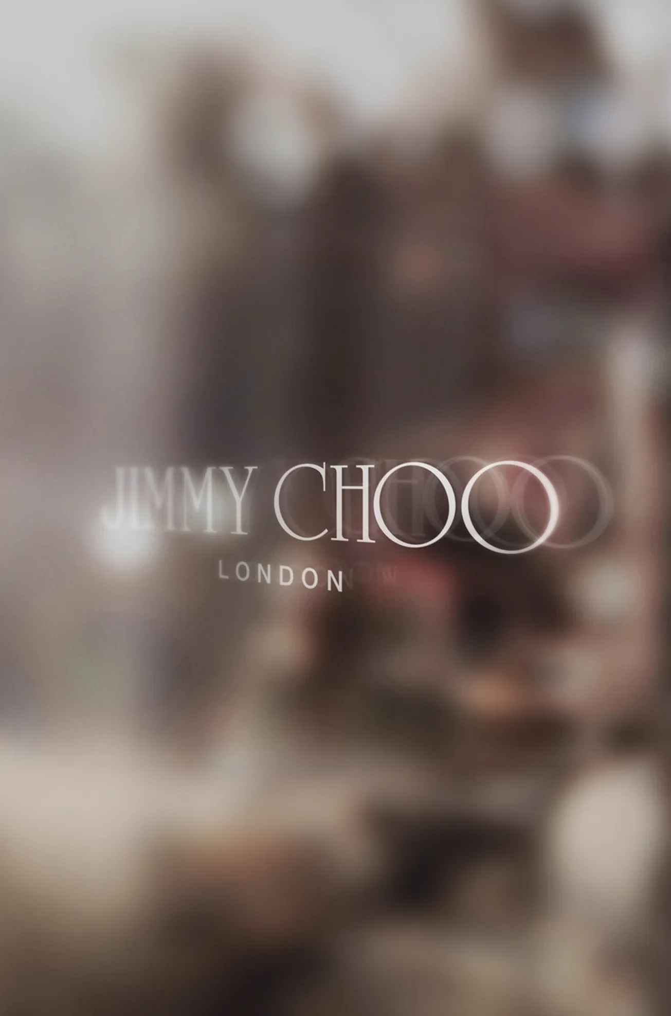 The Jimmy Choo London wordmark on a shopfront window, seen through glass.