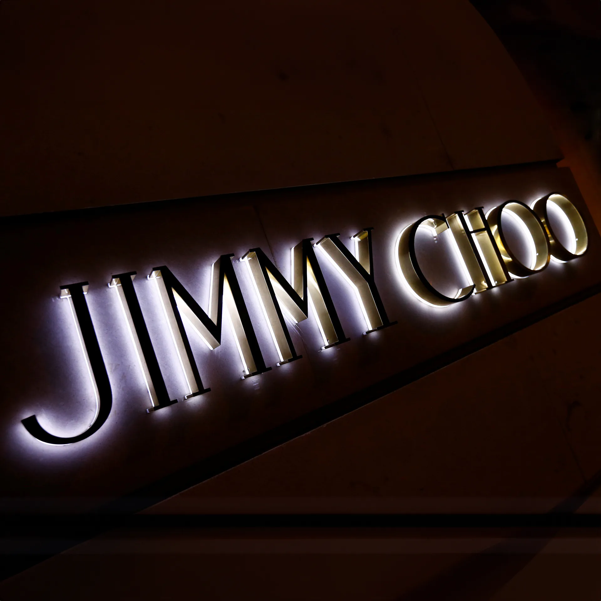 Illuminated Jimmy Choo lettering mounted on a dark wall.