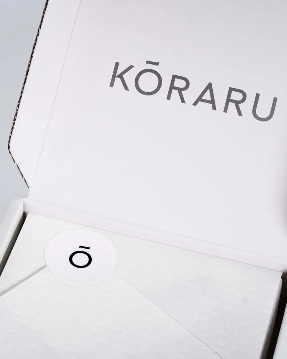An open Kōraru packaging box in white board, the wordmark across its lid.