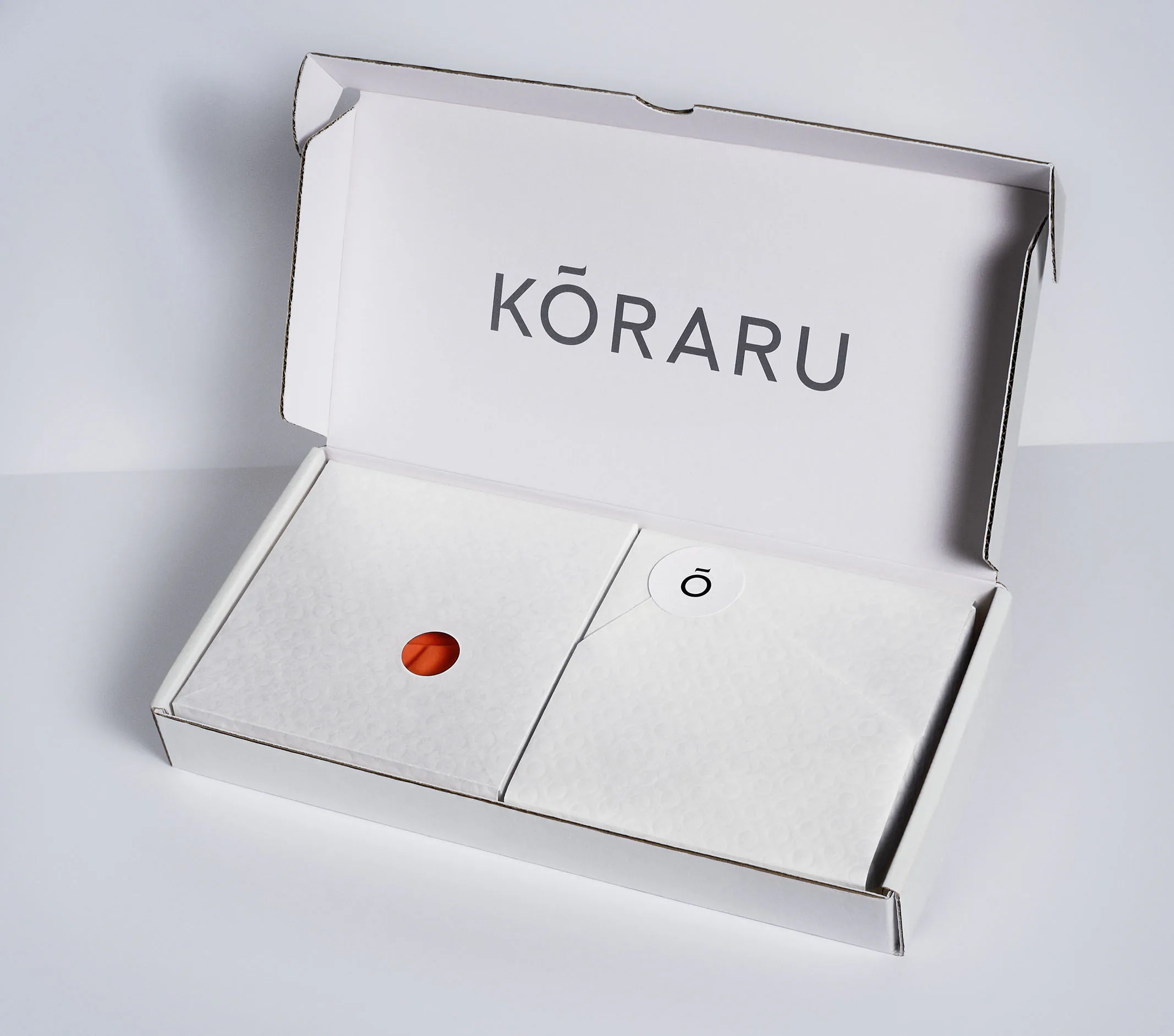 A Kōraru box open on a pale surface, a red seal on the tissue inside.