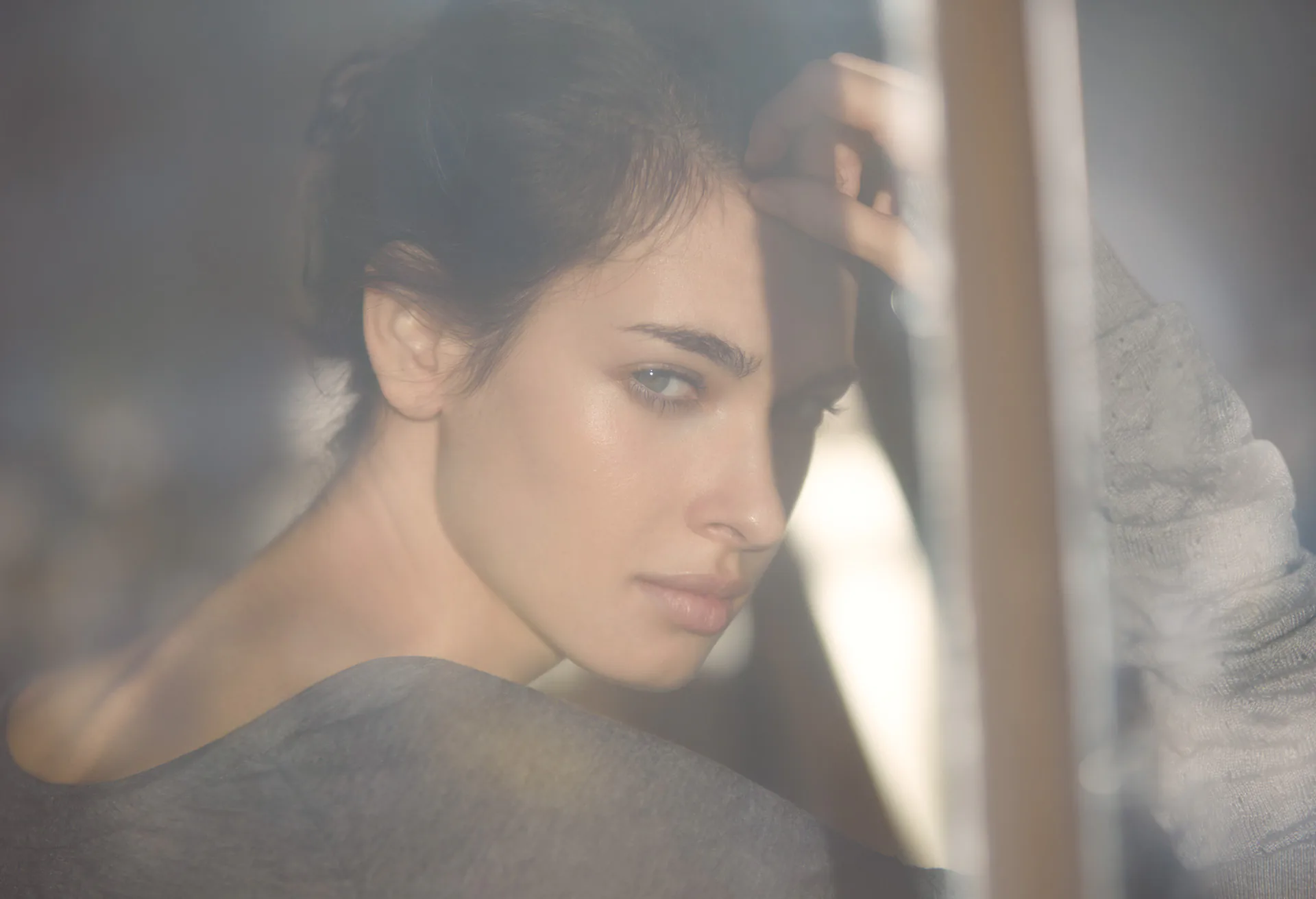 A portrait seen through misted glass, a woman resting her head against her raised arm.