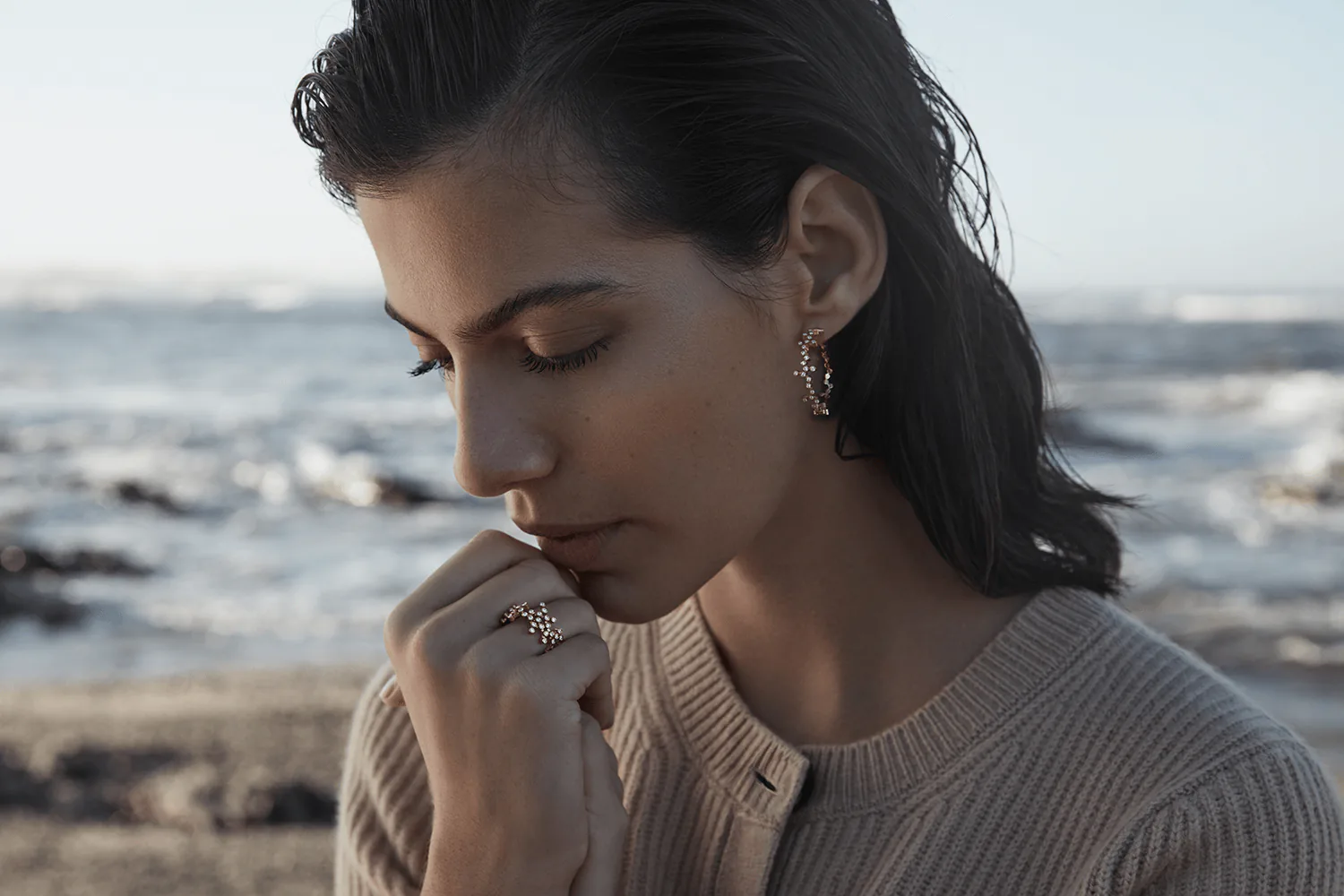 A model at the coast looking down, wearing filigree earrings and a ring.